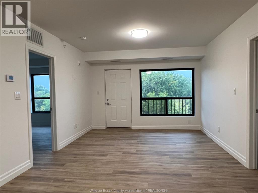 A spacious room with wooden flooring and a large window with a view of trees.