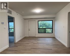 A spacious room with wooden flooring and a large window with a view of trees.