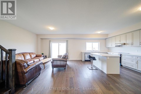A spacious living room with a brown leather couch and a white kitchen area.