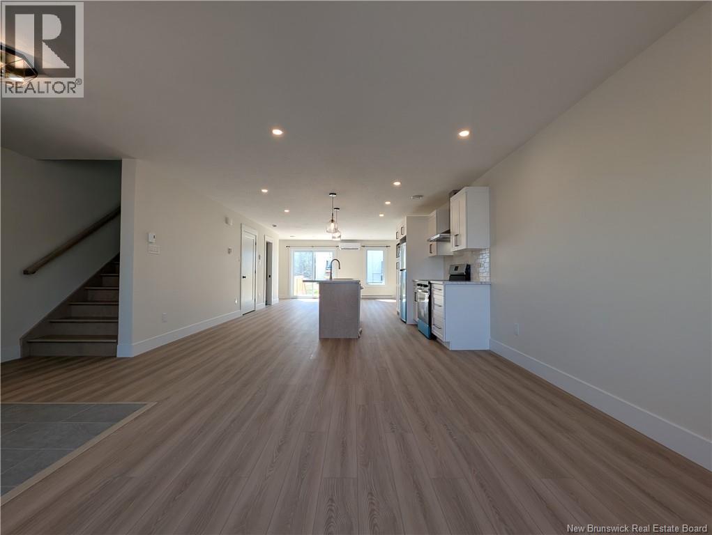 A spacious room with wooden flooring and a staircase on the left side.