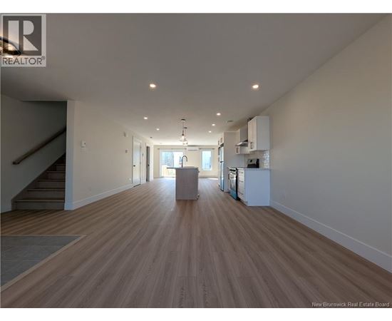 A spacious room with wooden flooring and a staircase on the left side.