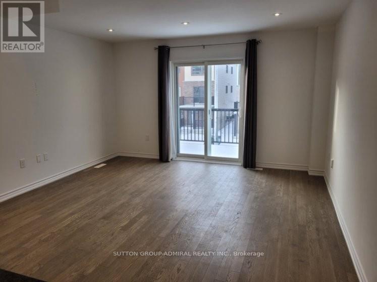 A spacious room with wooden flooring and a sliding glass door leading to a balcony.