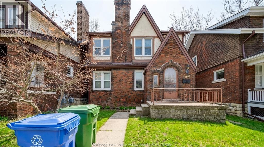 A blue recycling bin sits in front of a brick house.
