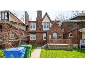 A blue recycling bin sits in front of a brick house.