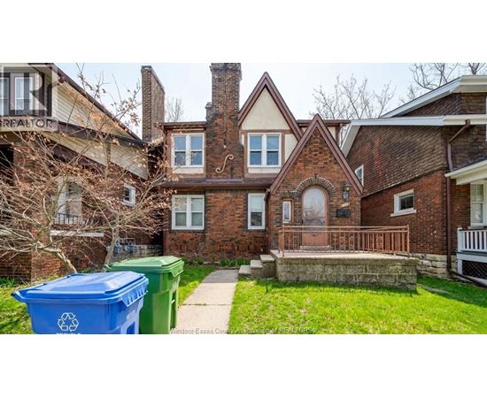 A blue recycling bin sits in front of a brick house.