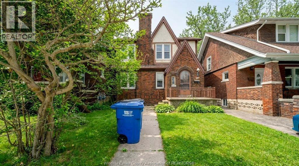 A blue trash bin sits on a grassy lawn in front of a house.