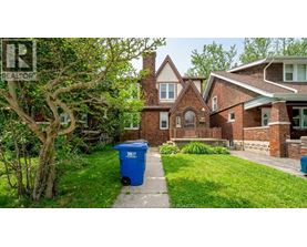 A blue trash bin sits on a grassy lawn in front of a house.