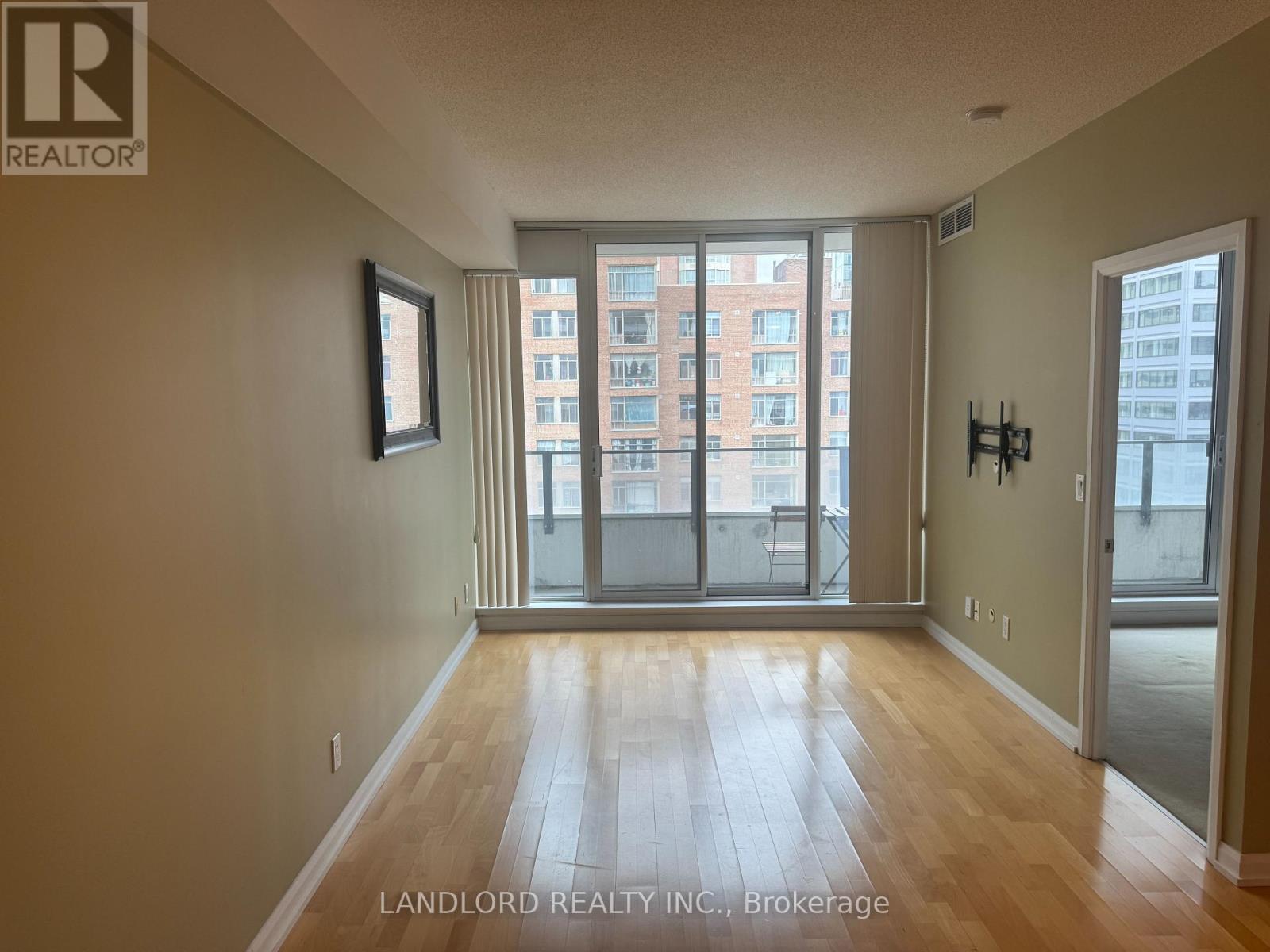 A room with wooden flooring and a view of a building through the windows.