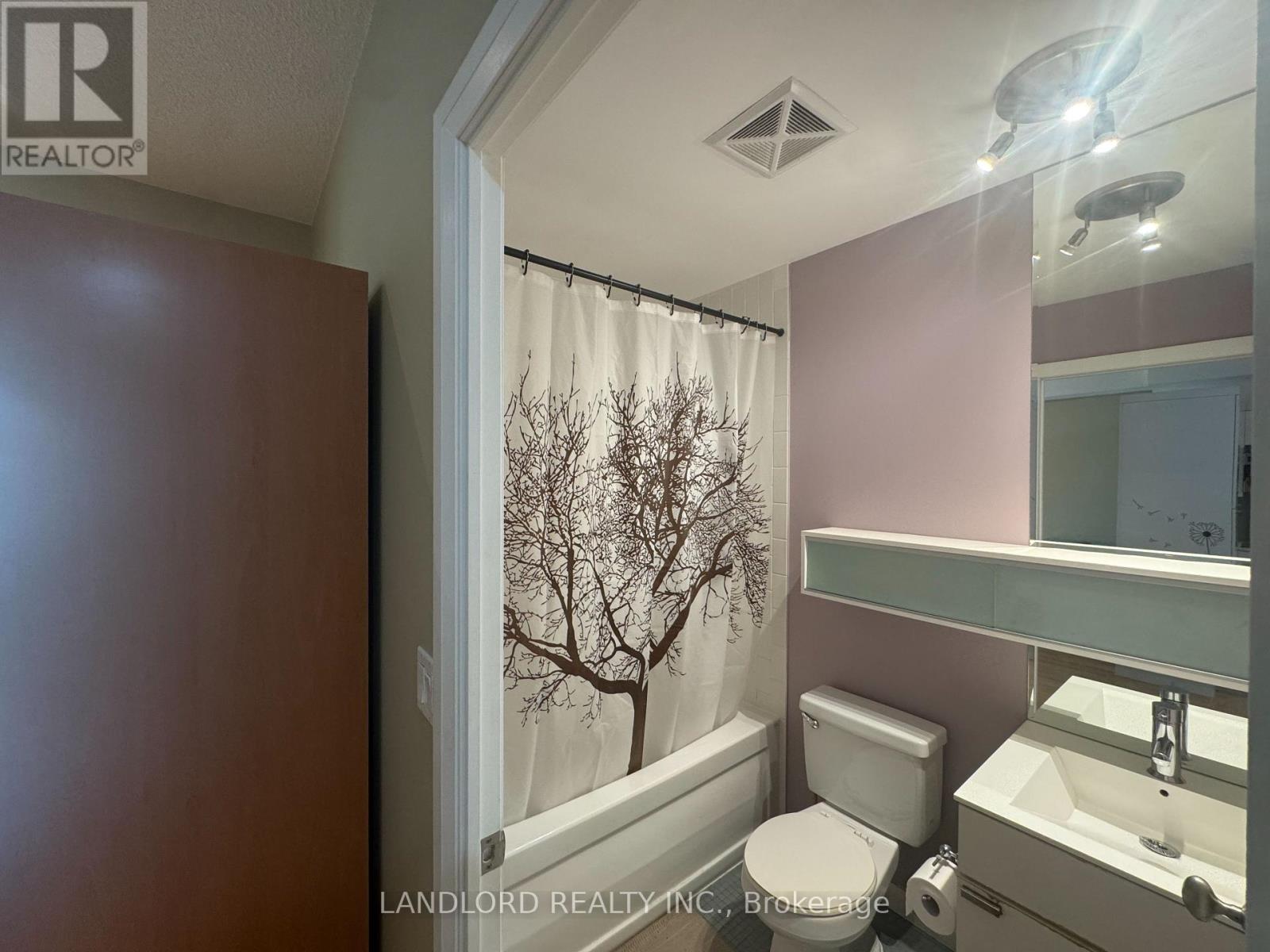A bathroom with a toilet, sink, and a window with a tree outside.