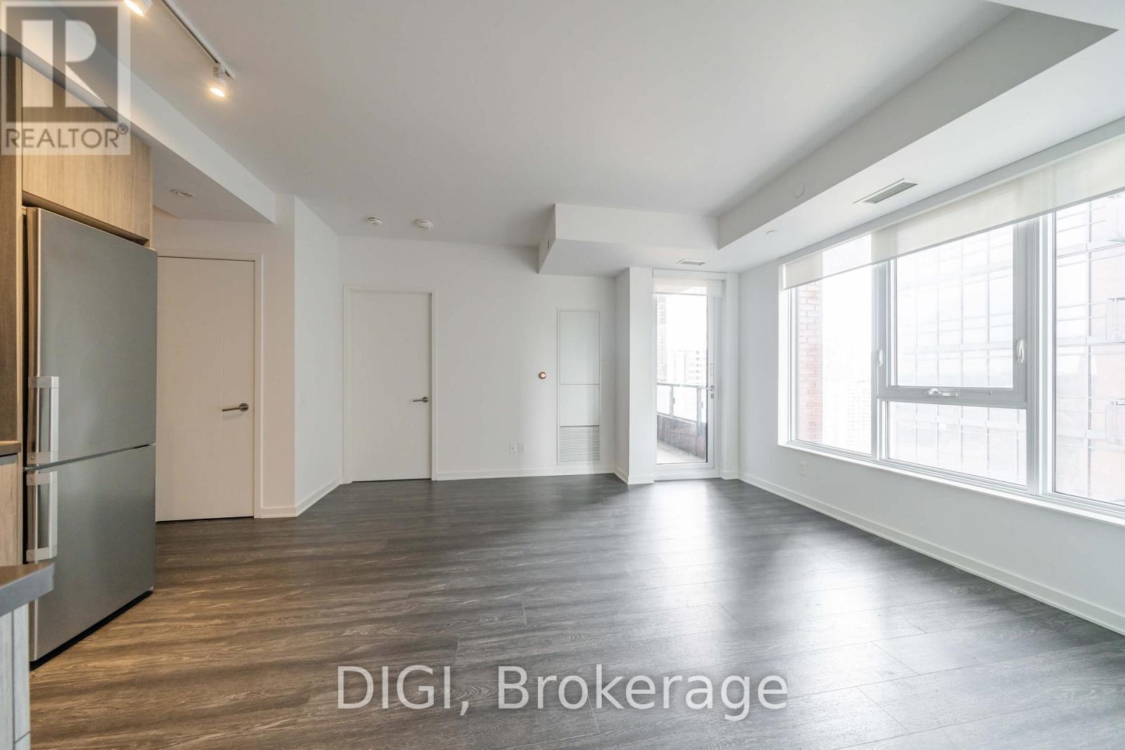 A spacious room with wooden flooring and large windows.