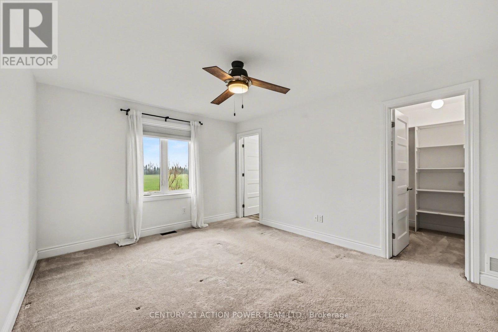 A bedroom with a ceiling fan and a window with curtains.