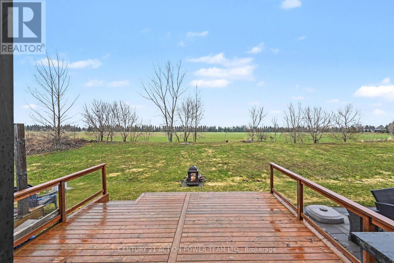 A wooden deck with a railing and a bench overlooking a grassy field.