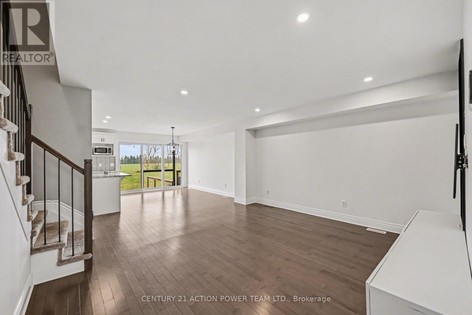 A spacious room with wooden flooring and a staircase on the left side.