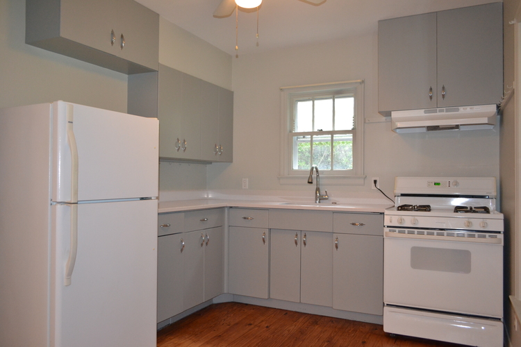 A white refrigerator is in a kitchen with wooden floors.