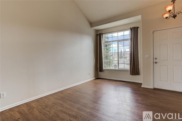 A room with wooden flooring and a large window with curtains.
