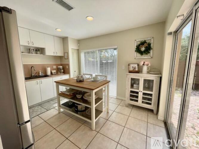 A kitchen with a refrigerator, a table with a woven top, and a window with blinds.