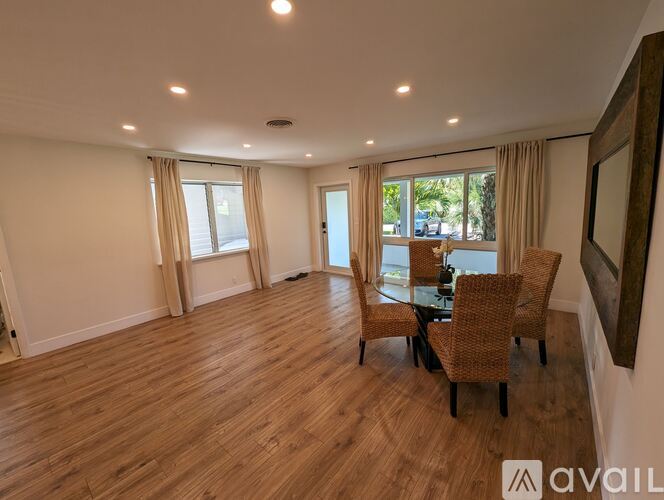 A spacious room with wooden floors and a glass table surrounded by chairs.