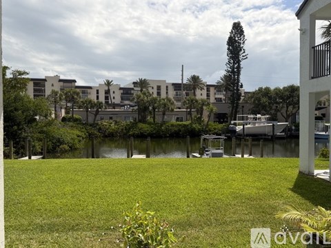 A grassy area in front of a row of buildings with a body of water in the foreground.