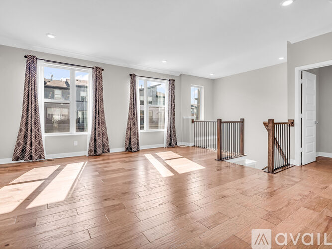 A spacious room with wooden flooring and large windows with curtains.
