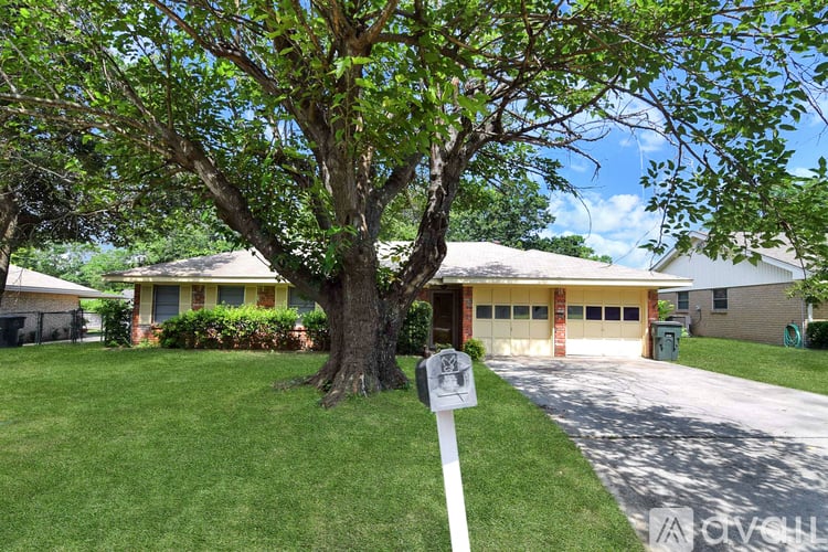 A tree stands in front of a house with a sign on a pole in front of it.