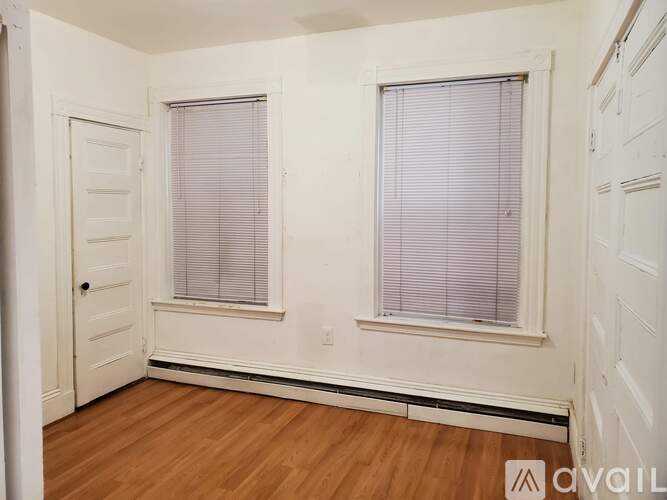 A room with wooden floors and two windows with blinds.