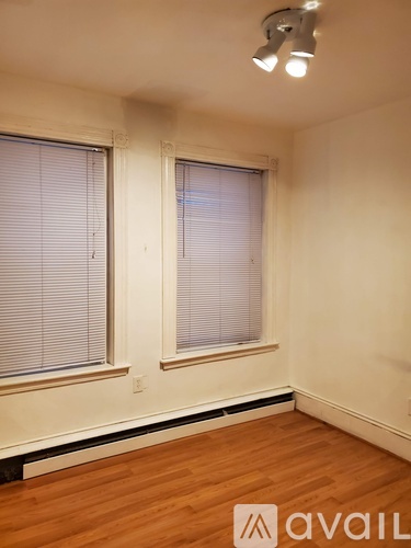 A room with wooden floors and two windows with blinds.