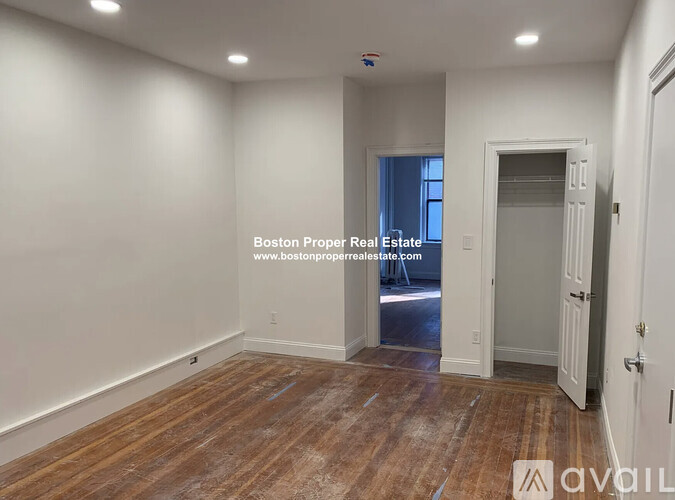 A room with wooden flooring and white walls, with a door leading to a hallway.
