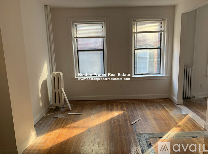 A room with wooden floors and two windows is available for rent.