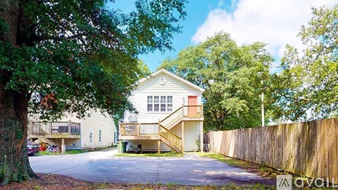 A house with a white facade and a red accent wall is surrounded by a wooden fence and trees.