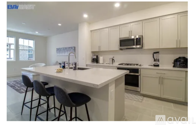 A kitchen with white cabinets and a white island with three black barstools.