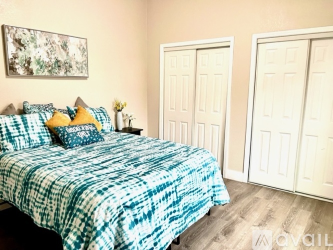 A bed with a blue and white comforter is in the foreground of a room with two white doors.