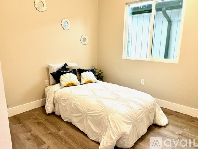 A bed with a white comforter and pillows in a room with a window.