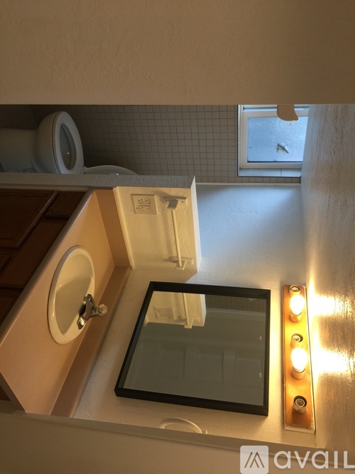 A bathroom with a toilet, sink, mirror, and lights.