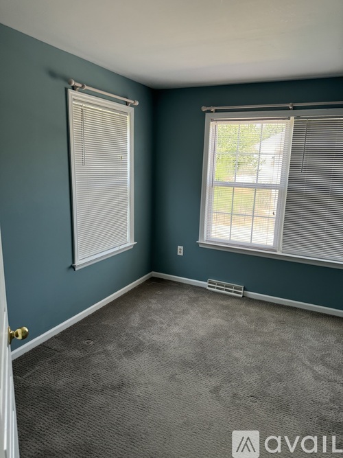 A room with a carpeted floor, a window with blinds, and a door with a gold handle.