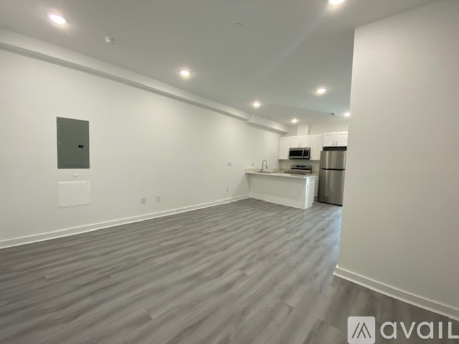 A spacious room with a grey floor and white walls, featuring a kitchen area with a refrigerator, oven, and sink.