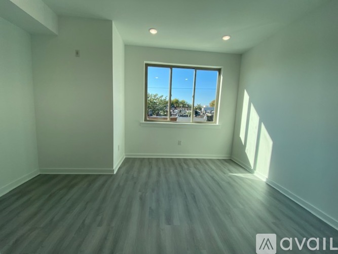 A spacious room with a large window and wooden flooring.