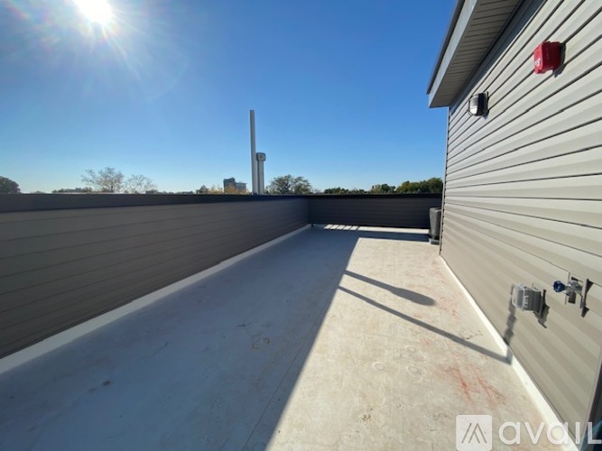 A sunny day on a rooftop with a metal pole and a building in the distance.