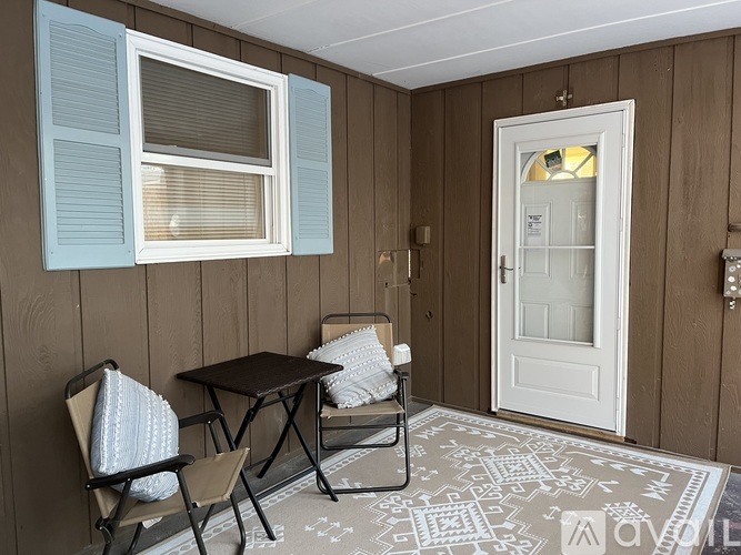 A small table with two chairs is in front of a wooden wall with a window and a door.