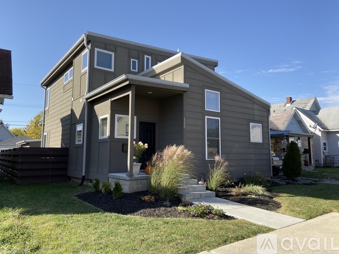 A grey house with a front yard and a clear blue sky.