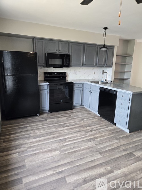 A kitchen with black appliances and wooden flooring.