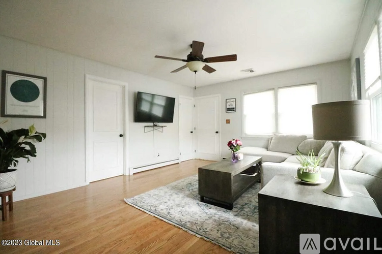A living room with a white couch, a coffee table, and a flat screen TV mounted on the wall.