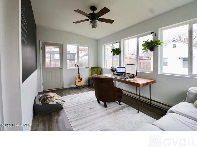 A room with a bed, a desk, a chair, a guitar, a ceiling fan, and a dog bed.