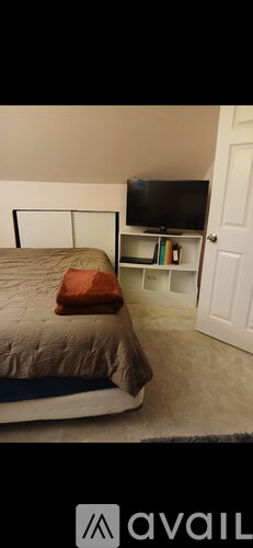 A bed with a pillow and a television on a stand in a room.
