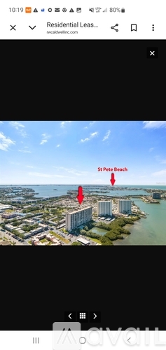 A modern building with a pool in front is surrounded by other buildings and a body of water.