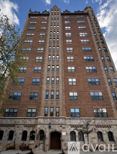 A tall red brick building with many windows and a tree in front.