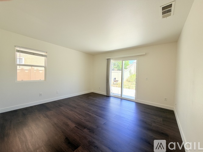 A spacious room with wooden floors and three windows.