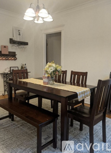 A brown wooden dining table with four chairs and a vase of flowers on top.