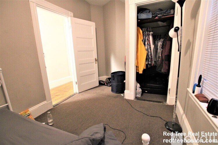 A bedroom with a grey carpet and a wardrobe with clothes hanging out.