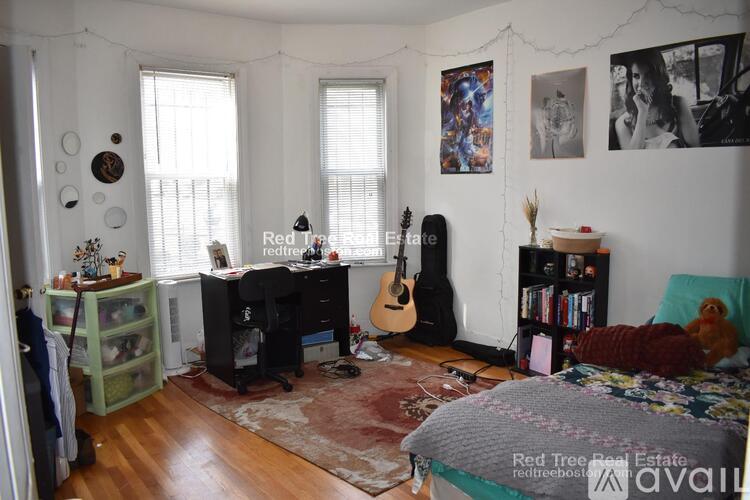 A room with a guitar, a desk, and a bed.