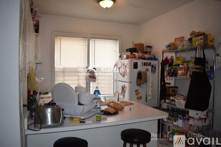 A kitchen with a white fridge, a white counter, and a white stool.
